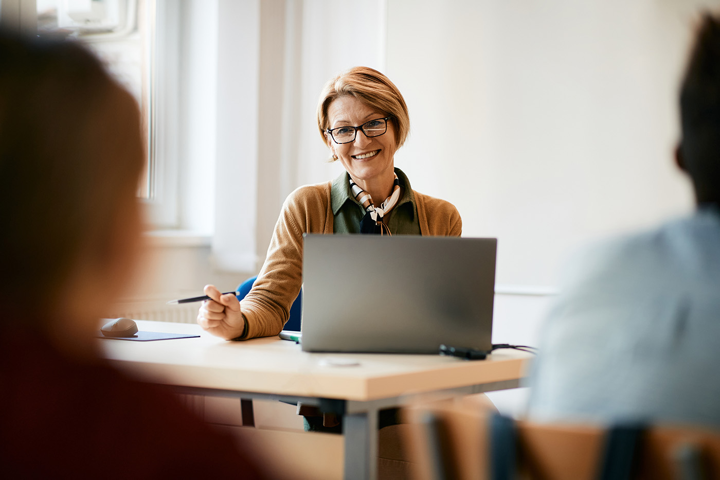 Eine Lehrerin sitzt am Laptop und blickt in ihre Klasse.